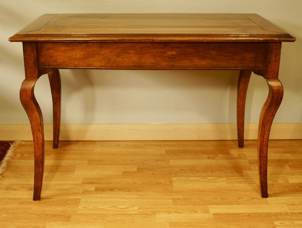 An antique French walnut writing table featuring three frieze drawers, brass handles, and cabriole legs against a carved wooden panelled backdrop. View III