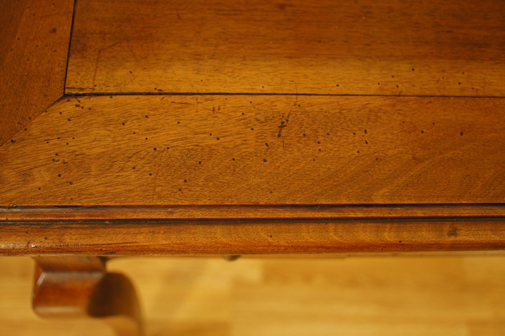 An antique French walnut writing table featuring three frieze drawers, brass handles, and cabriole legs against a carved wooden panelled backdrop. View VII