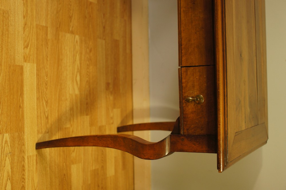 An antique French walnut writing table featuring three frieze drawers, brass handles, and cabriole legs against a carved wooden panelled backdrop. View XII