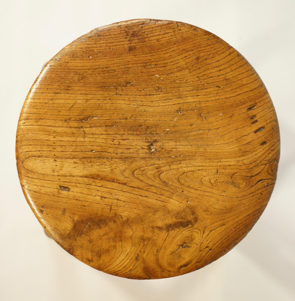 An antique wooden stool featuring a circular solid elm seat resting upon four splayed turned legs joined by an X-frame stretcher. View II
