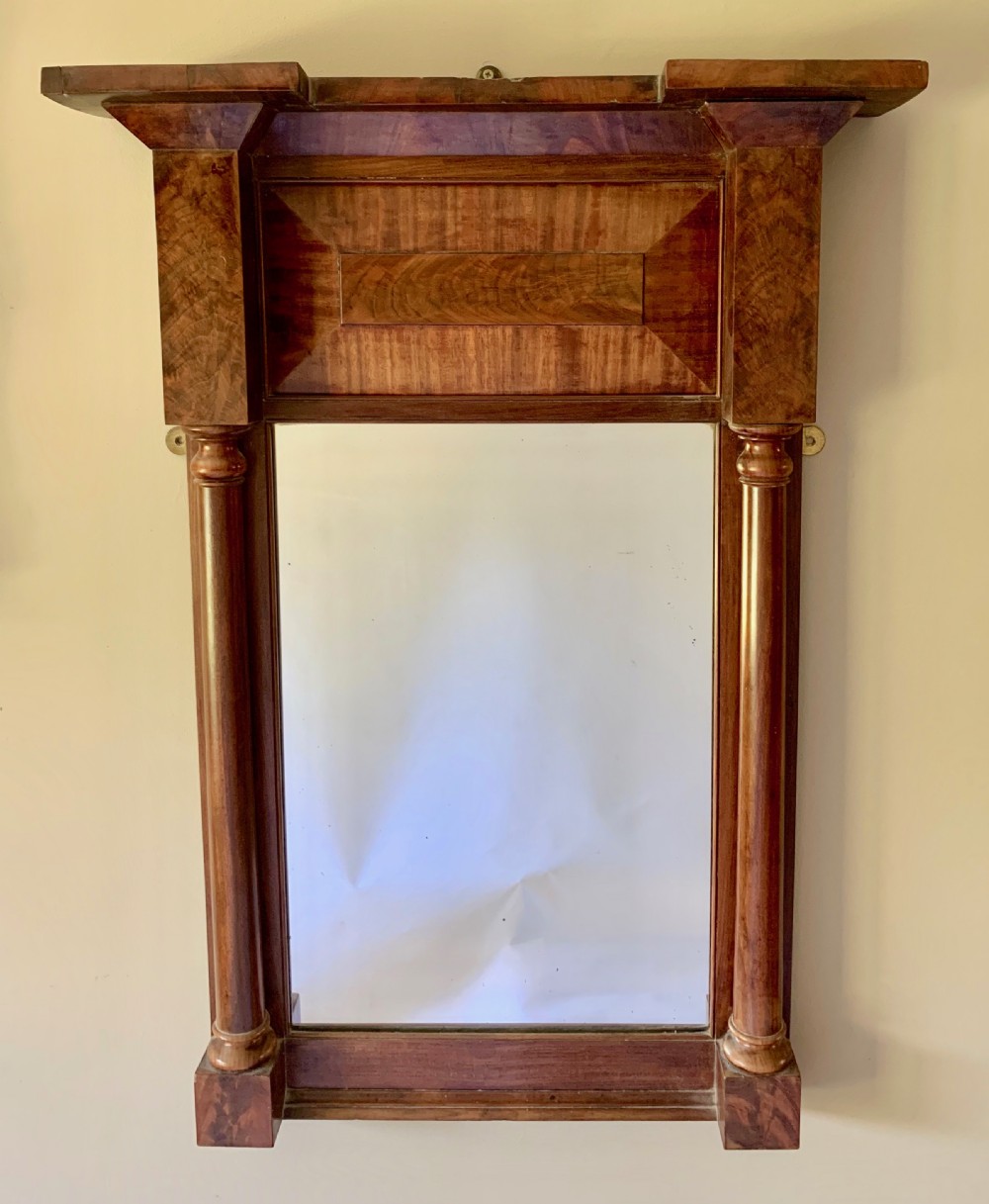 A Regency mahogany pier mirror featuring an upper frieze with flame mahogany veneer, flanked by turned half-columns and topped with a projecting cornice.