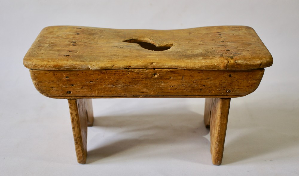 A low rustic pine stool with a hand-cut central handle aperture and two slab legs.