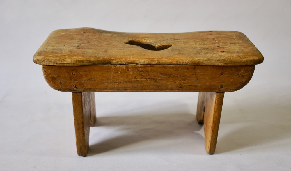 A low rustic pine stool with a hand-cut central handle aperture and two slab legs. View II