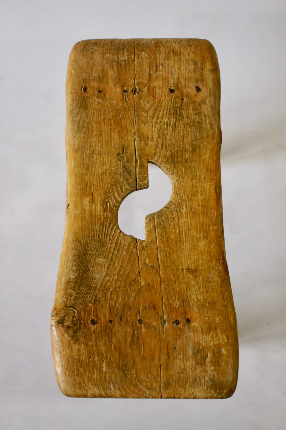 A low rustic pine stool with a hand-cut central handle aperture and two slab legs. View III