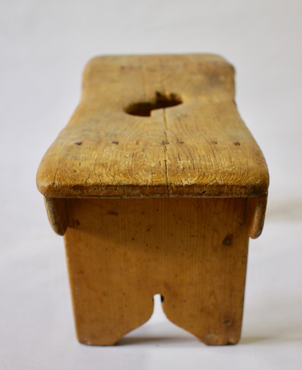 A low rustic pine stool with a hand-cut central handle aperture and two slab legs. View IV