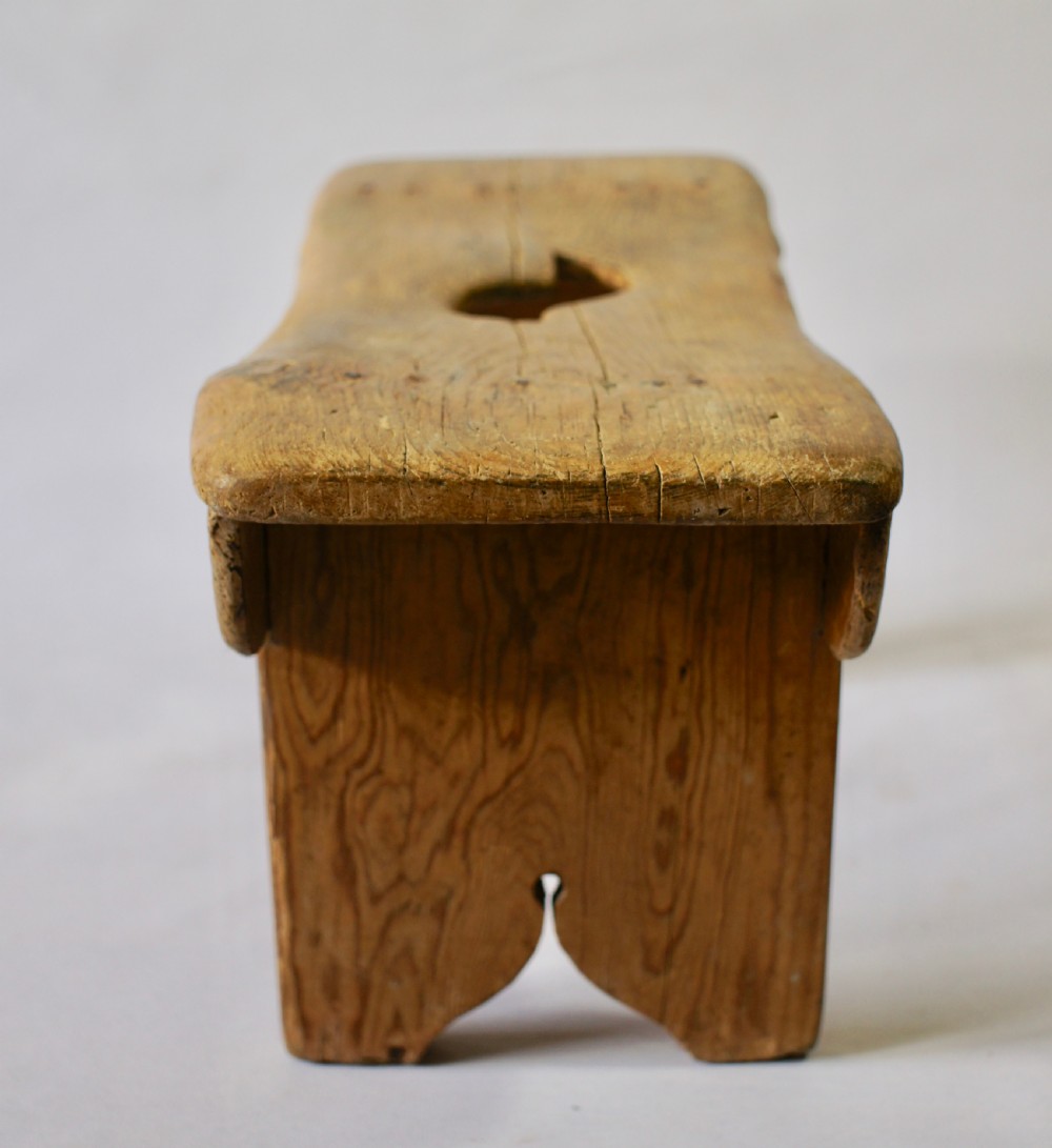 A low rustic pine stool with a hand-cut central handle aperture and two slab legs. View V