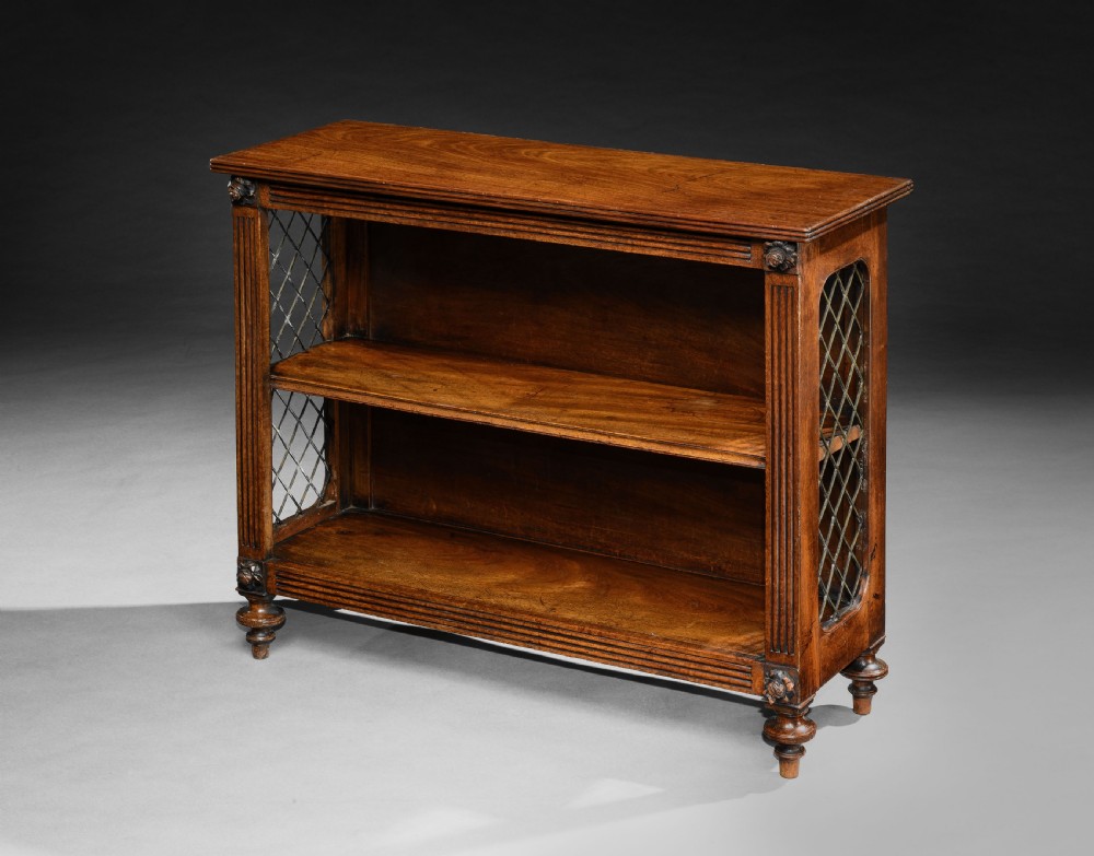 A Regency mahogany open dwarf bookcase featuring two shelves, fluted side pilasters with carved rosettes, brass trellis side panels, and turned feet.