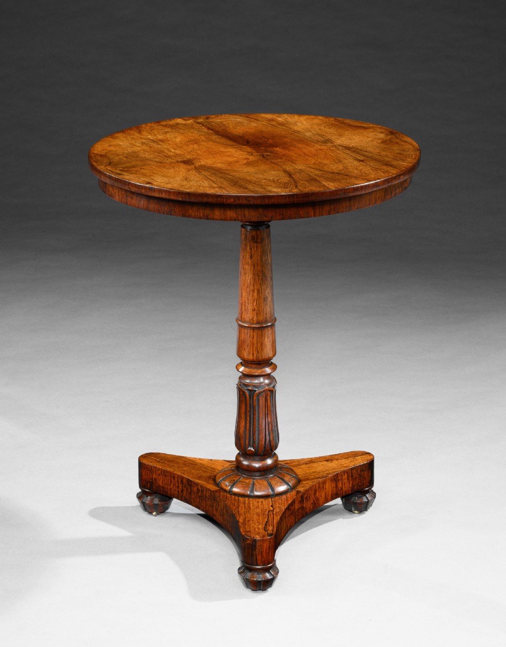 A George IV rosewood occasional table with a circular top, turned central pedestal stem, and a triform base with carved feet.