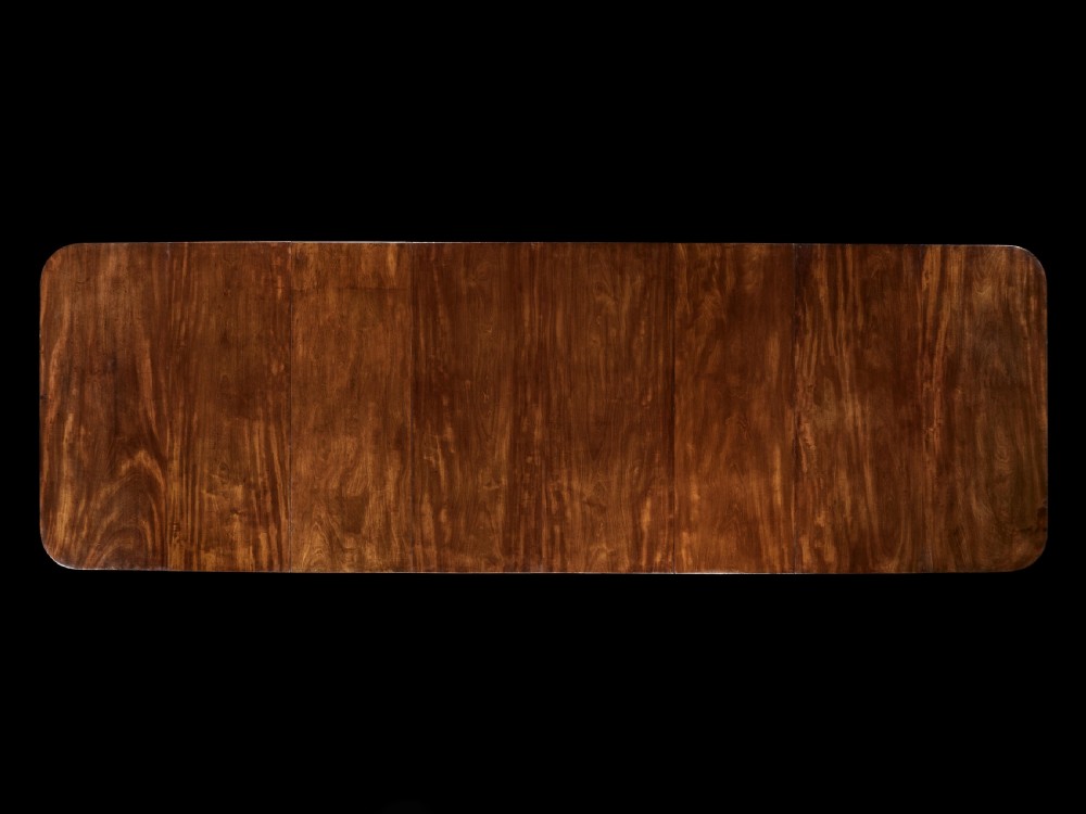 A long George III mahogany dining table featuring three reeded pedestal bases with splayed legs and brass castors. View II