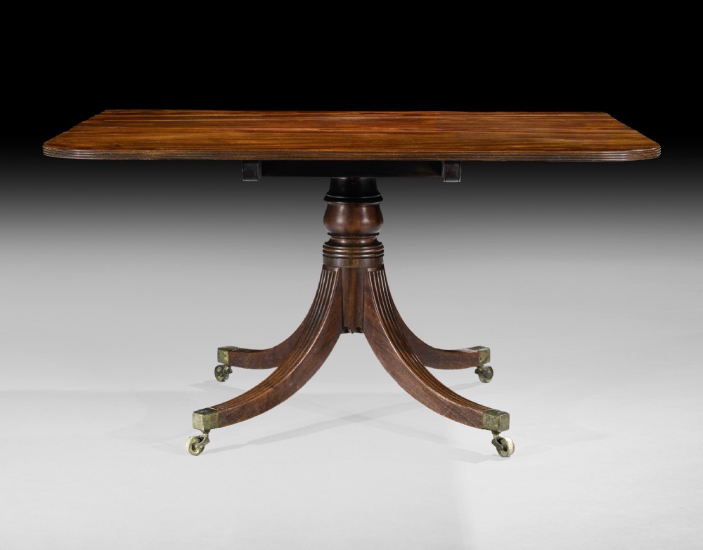 A long George III mahogany dining table featuring three reeded pedestal bases with splayed legs and brass castors. View III
