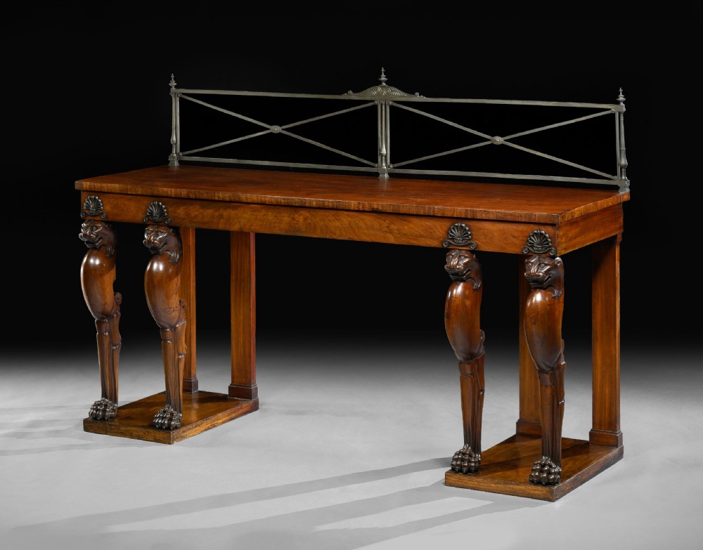 An Irish Regency mahogany serving table featuring four carved lion monopodium legs, dual plinth bases, and a brass gallery rail.