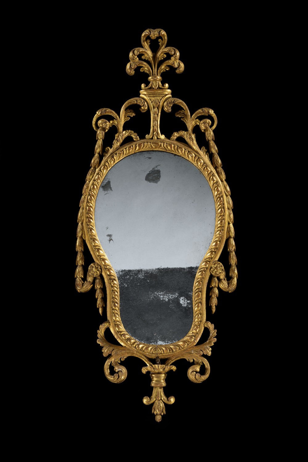 An 18th-century Neoclassical carved giltwood wall mirror featuring husk swags, a scrolling cresting, and an antiqued glass plate.