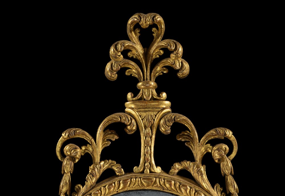 An 18th-century Neoclassical carved giltwood wall mirror featuring husk swags, a scrolling cresting, and an antiqued glass plate. View V