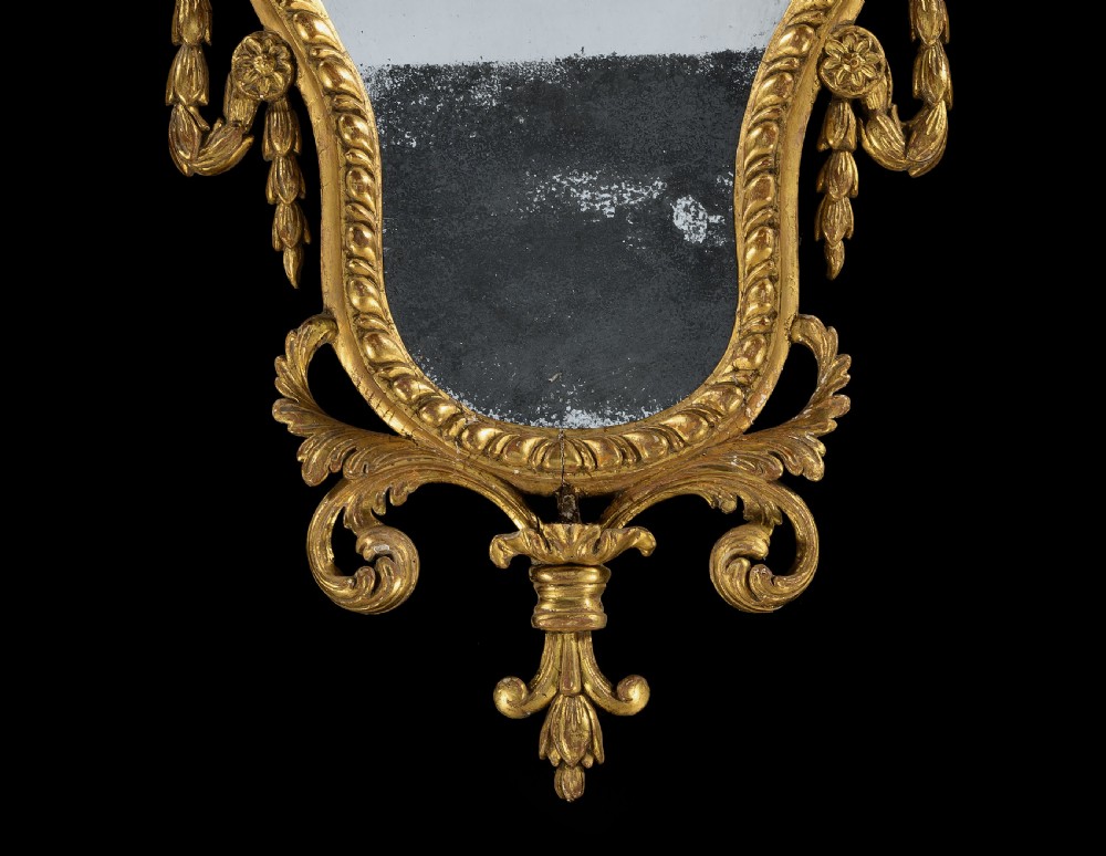 An 18th-century Neoclassical carved giltwood wall mirror featuring husk swags, a scrolling cresting, and an antiqued glass plate. View VI