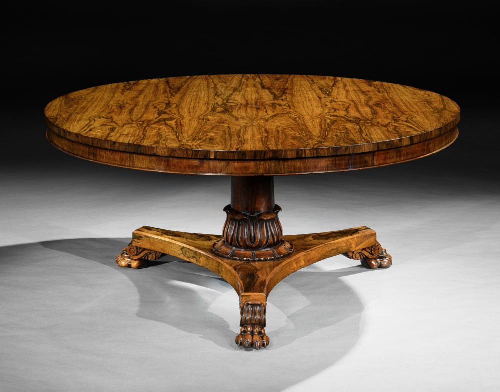 A large circular George IV rosewood centre table featuring a figured timber top resting on a carved pedestal column and a triform base with paw feet.