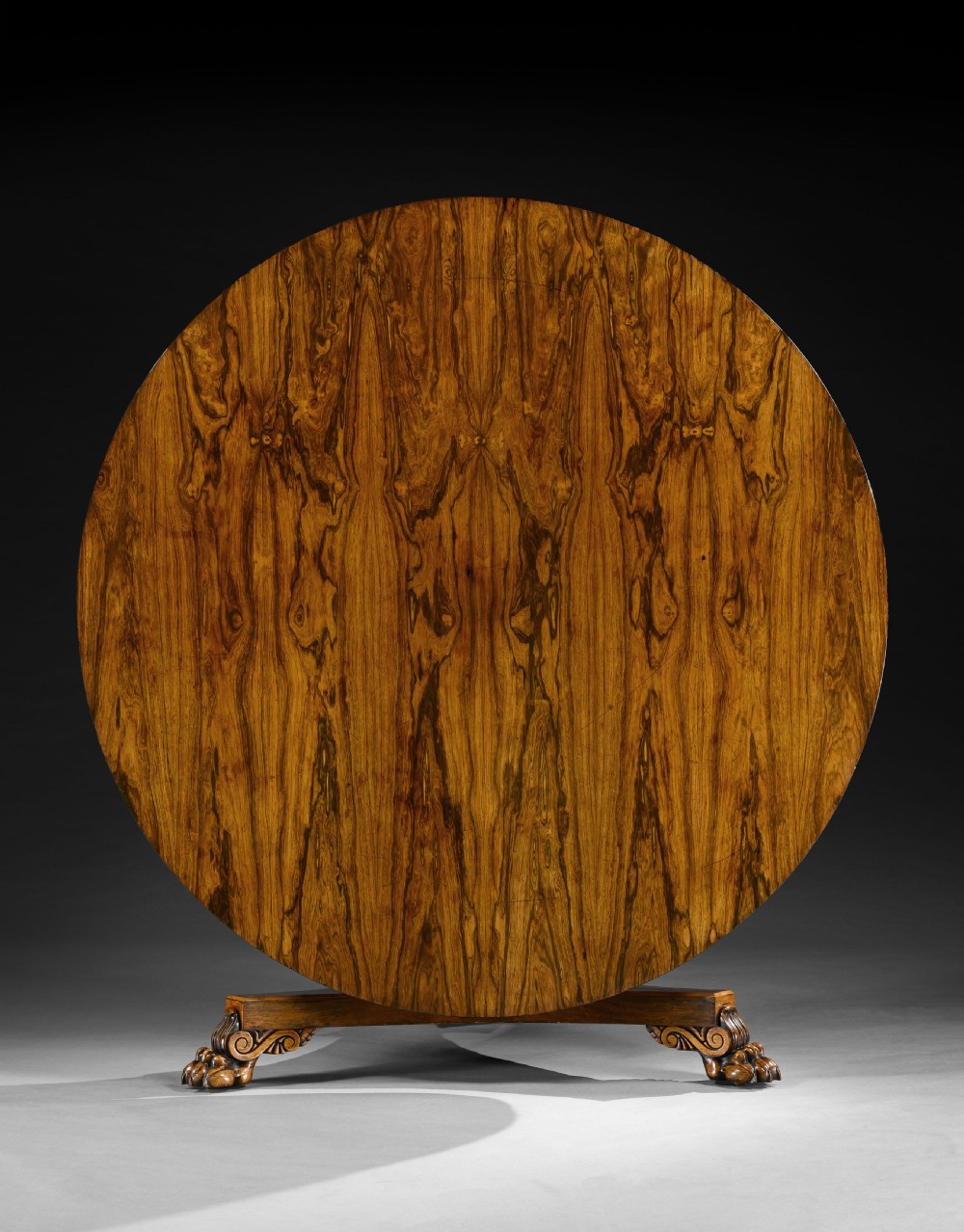 A large circular George IV rosewood centre table featuring a figured timber top resting on a carved pedestal column and a triform base with paw feet. View II