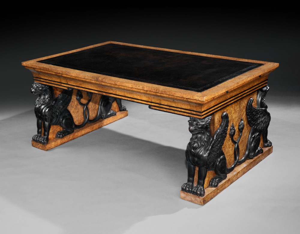 A Regency burr oak partners desk featuring a black leather writing top supported by carved ebonised winged griffins on plinth bases.