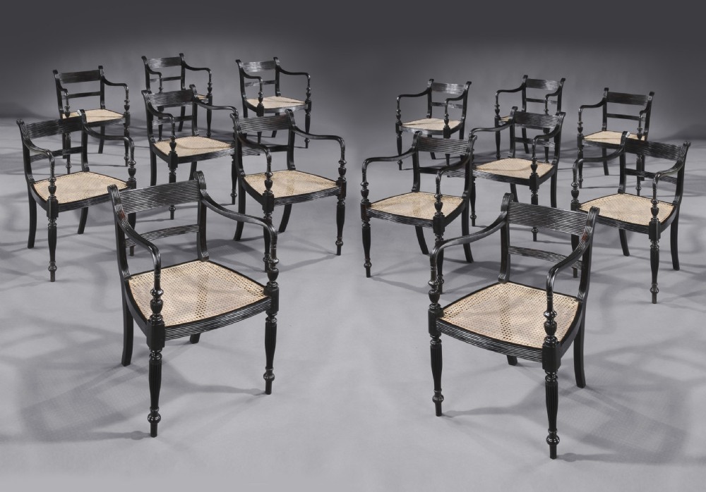 A set of fourteen carved black ebony armchairs featuring reeded top rails, hand-woven cane seats, and turned front legs.