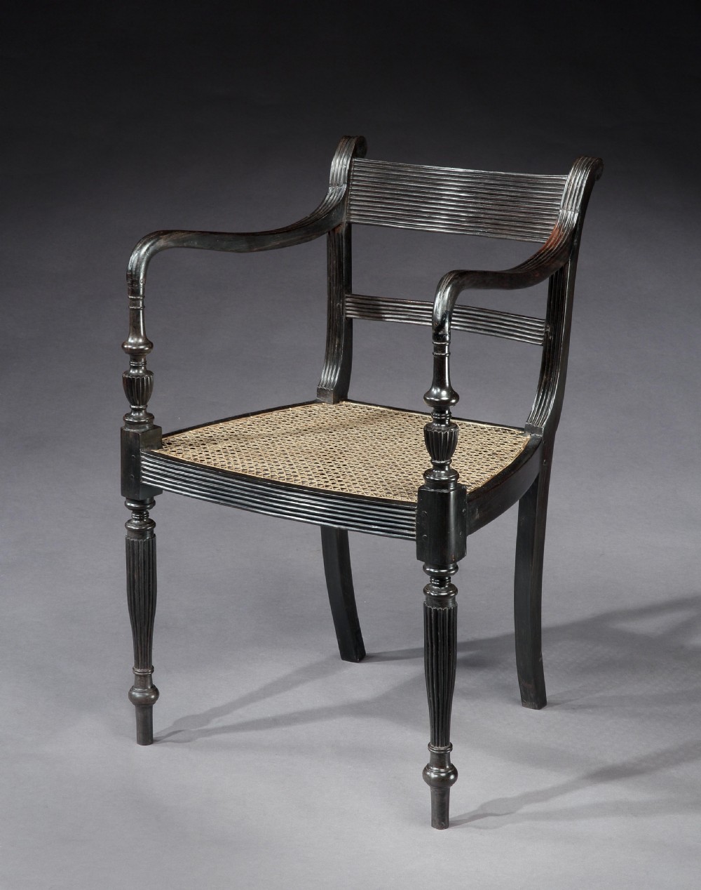 A set of fourteen carved black ebony armchairs featuring reeded top rails, hand-woven cane seats, and turned front legs. View II