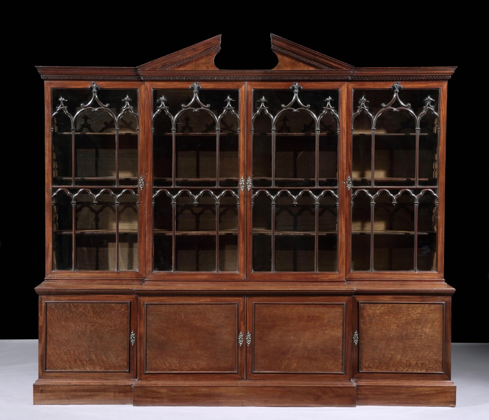 A large George III mahogany breakfront bookcase featuring a broken pediment, four Gothic astragal-glazed upper doors, and four solid mahogany cupboard doors below.