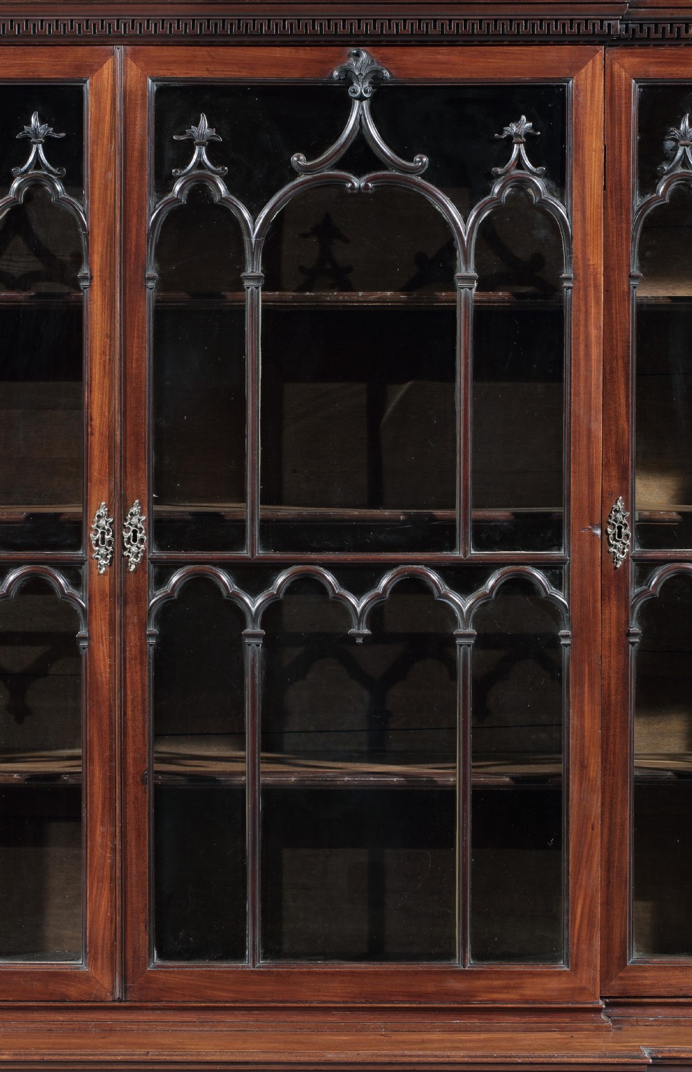 A large George III mahogany breakfront bookcase featuring a broken pediment, four Gothic astragal-glazed upper doors, and four solid mahogany cupboard doors below. View II