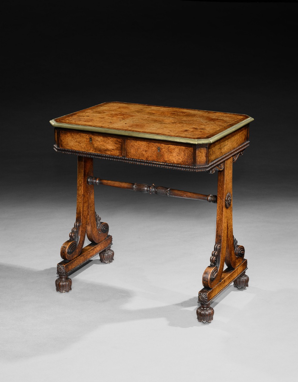 A Regency pollard oak writing table featuring a rectangular figured top, two frieze drawers, carved trestle supports, and a turned central stretcher.
