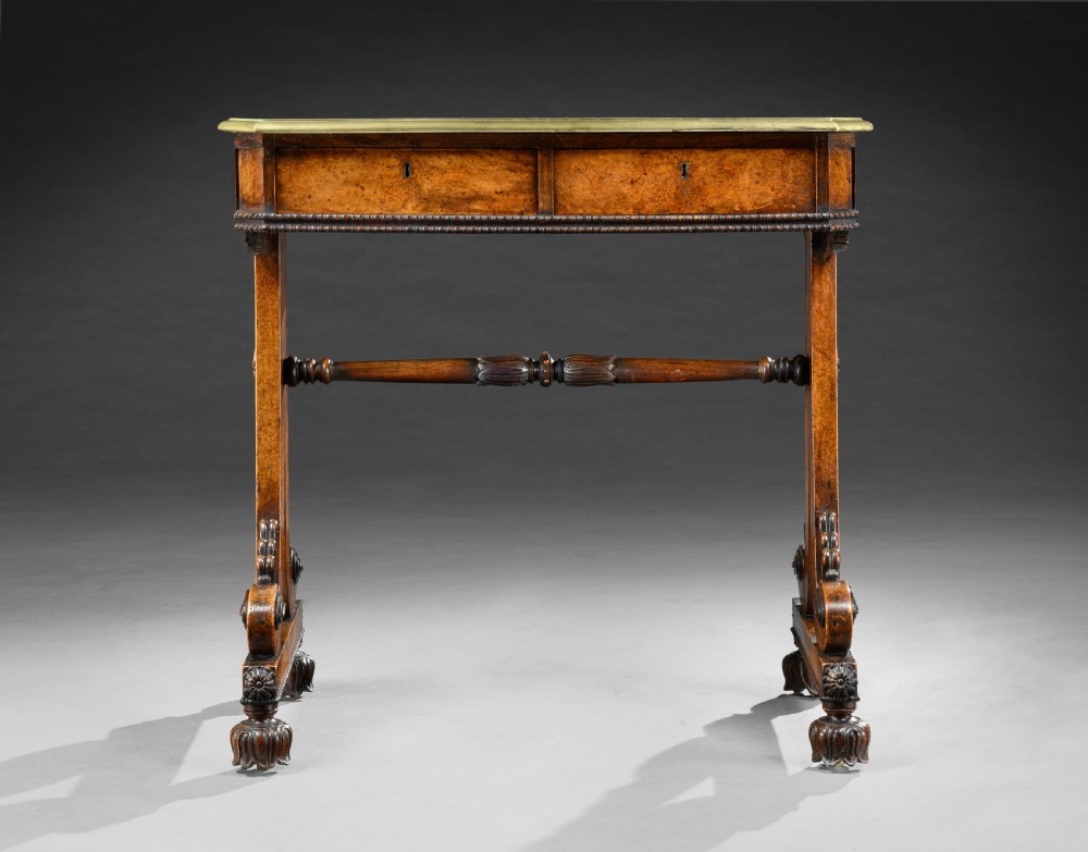 A Regency period pollard oak writing table featuring two frieze drawers, carved scroll trestle legs, a turned central stretcher, and carved feet. View II