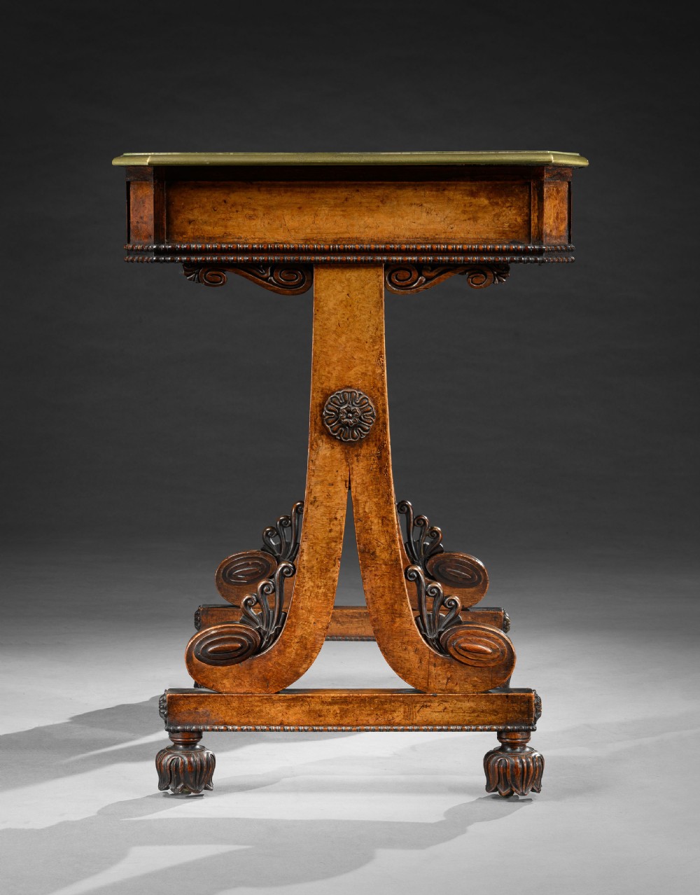 A Regency period pollard oak writing table featuring two frieze drawers, carved scroll trestle legs, a turned central stretcher, and carved feet. View III
