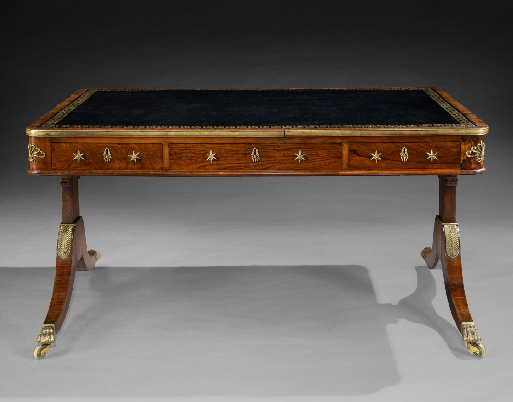 A Regency style rosewood writing table featuring a dark leather inset top with gilt Greek key tooling, brass star mounts along the frieze, and trestle legs on brass paw castors. View II