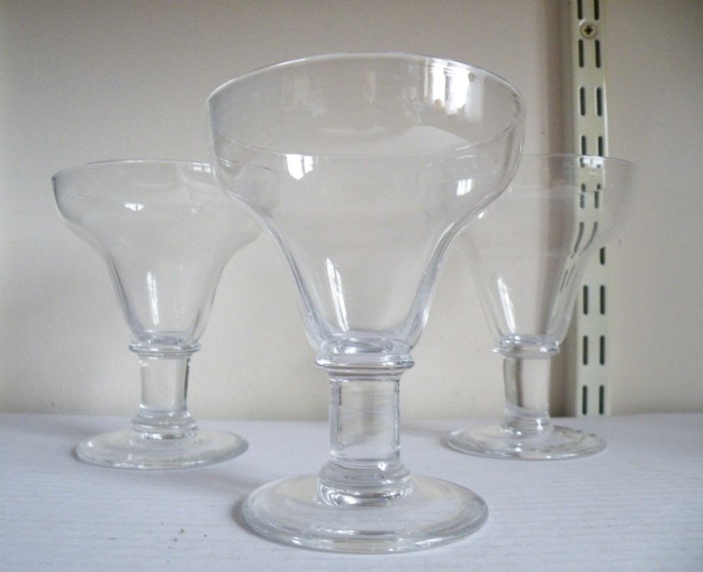 A set of three clear antique glass rummers featuring pan-topped flared bowls, short knopped stems, and circular flat bases.