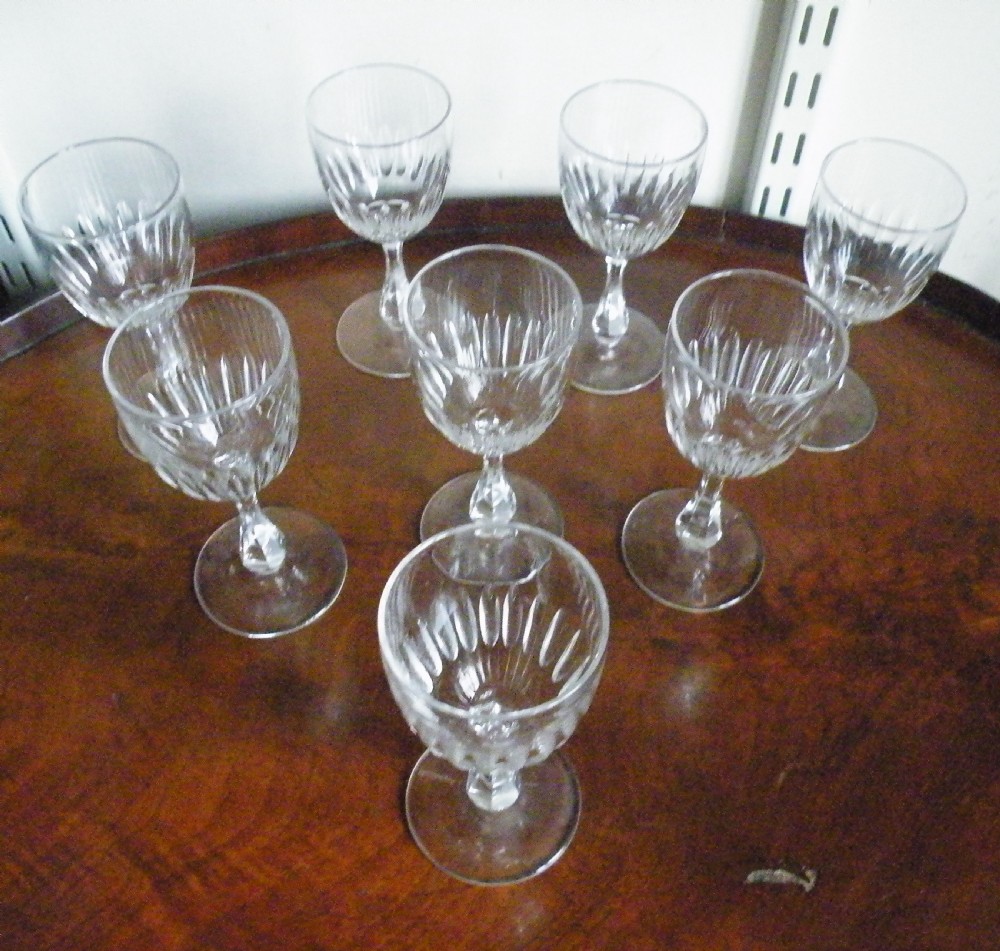 A set of eight Victorian clear cut glass sherry glasses featuring fluted bowls and slender stems arranged on a polished wood surface. View II