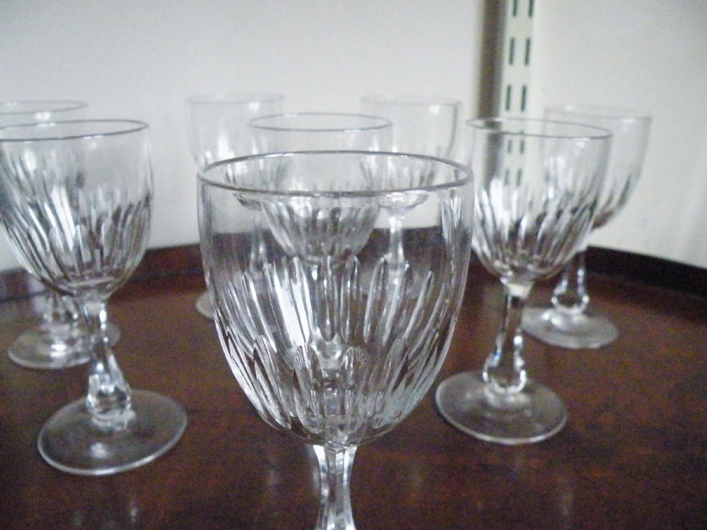 A set of eight Victorian clear cut glass sherry glasses featuring fluted bowls and slender stems arranged on a polished wood surface. View IV