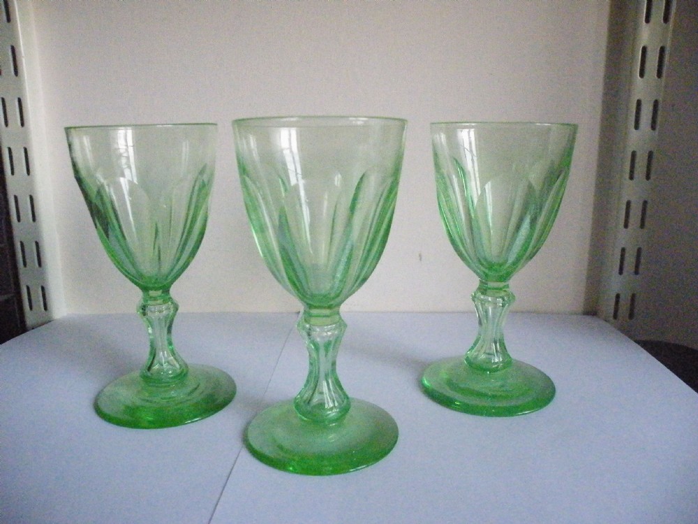 Three nineteenth-century light green vaseline glass wine glasses featuring panelled bowls and knopped stems.