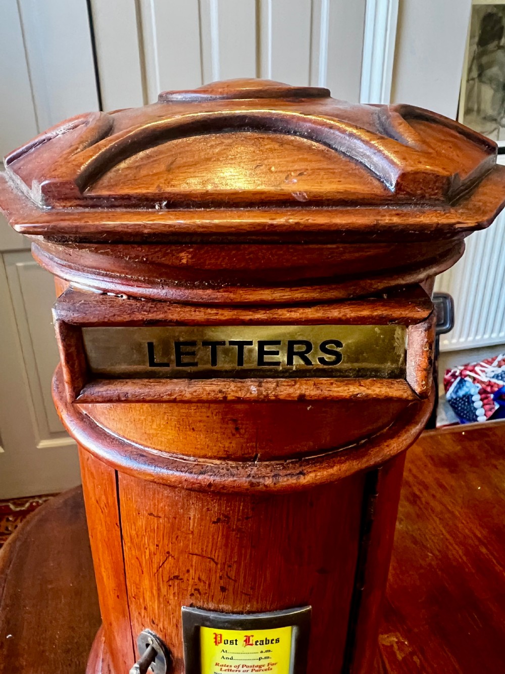 A cylindrical wooden post box featuring a brass letter slot, a small door with a key, and a lower drawer with a metal handle. View IV