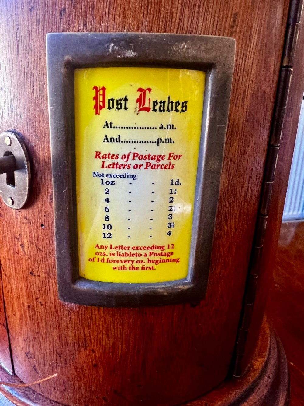 A cylindrical wooden post box featuring a brass letter slot, a small door with a key, and a lower drawer with a metal handle. View V