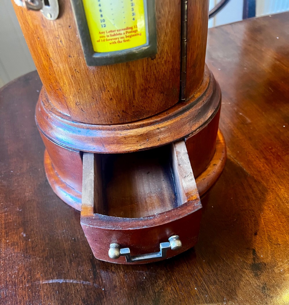 A cylindrical wooden post box featuring a brass letter slot, a small door with a key, and a lower drawer with a metal handle. View VIII