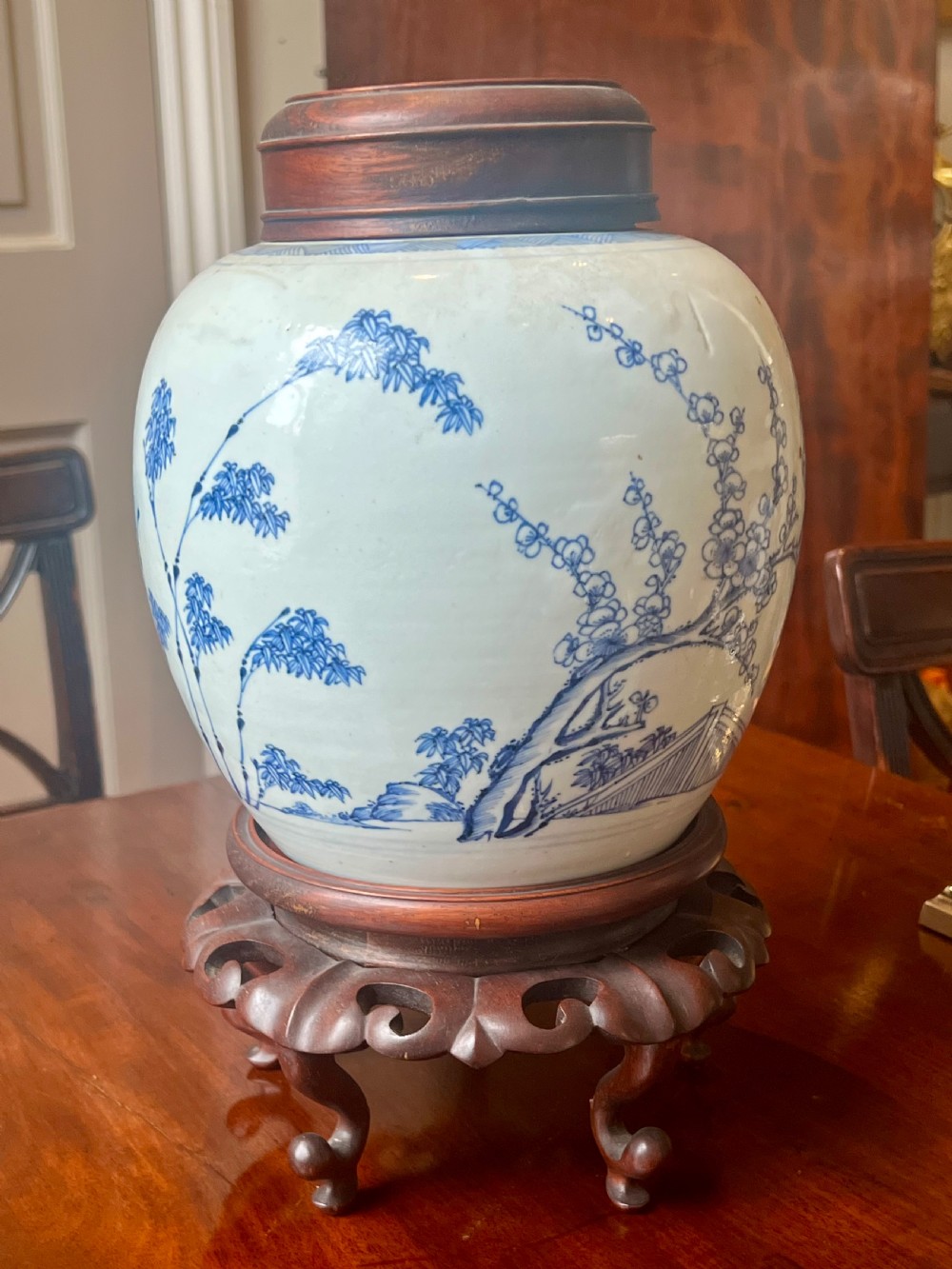 A blue and white porcelain ginger jar featuring hand-painted botanical motifs, complete with a wooden cover and resting on an intricately carved wooden stand. View IV