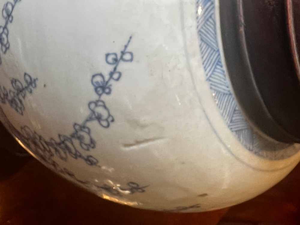 A blue and white porcelain ginger jar featuring hand-painted botanical motifs, complete with a wooden cover and resting on an intricately carved wooden stand. View V