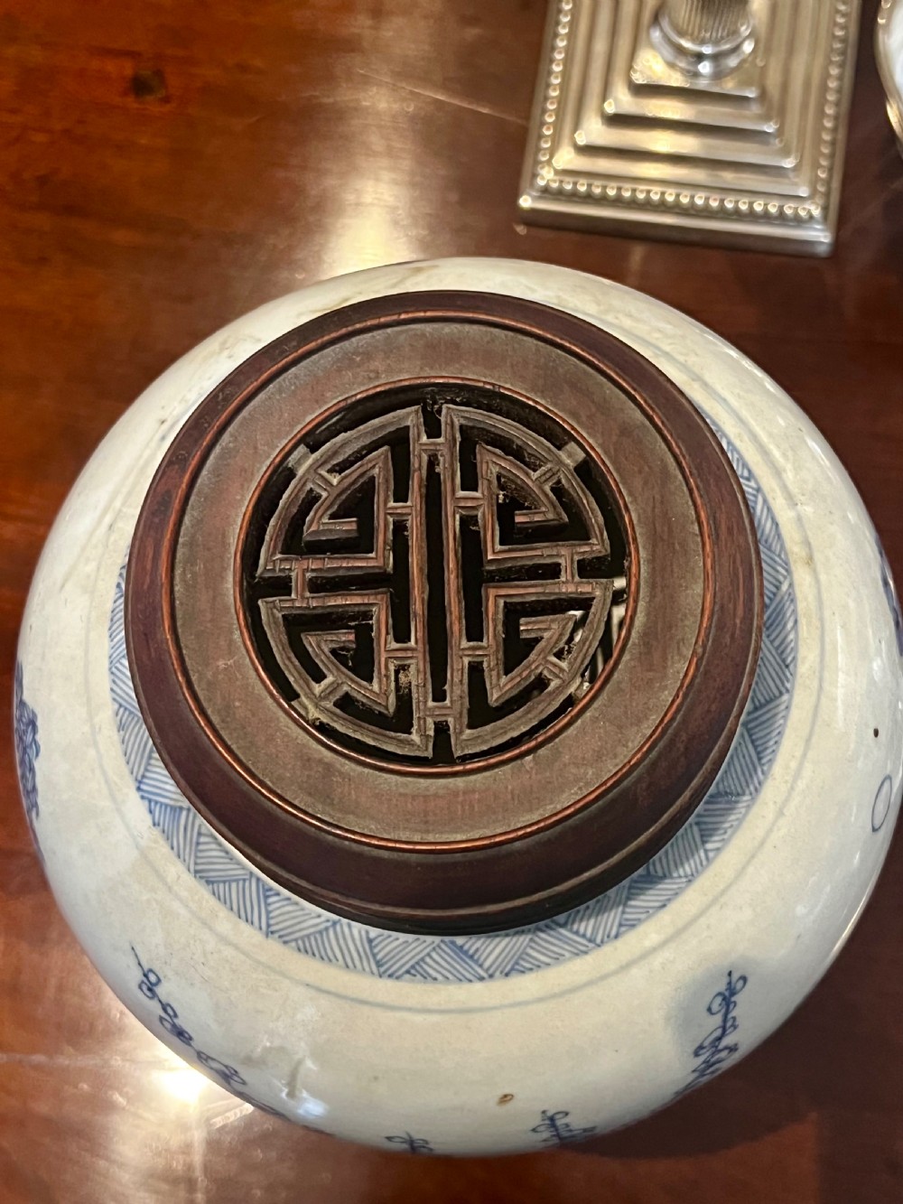 A blue and white porcelain ginger jar featuring hand-painted botanical motifs, complete with a wooden cover and resting on an intricately carved wooden stand. View VII