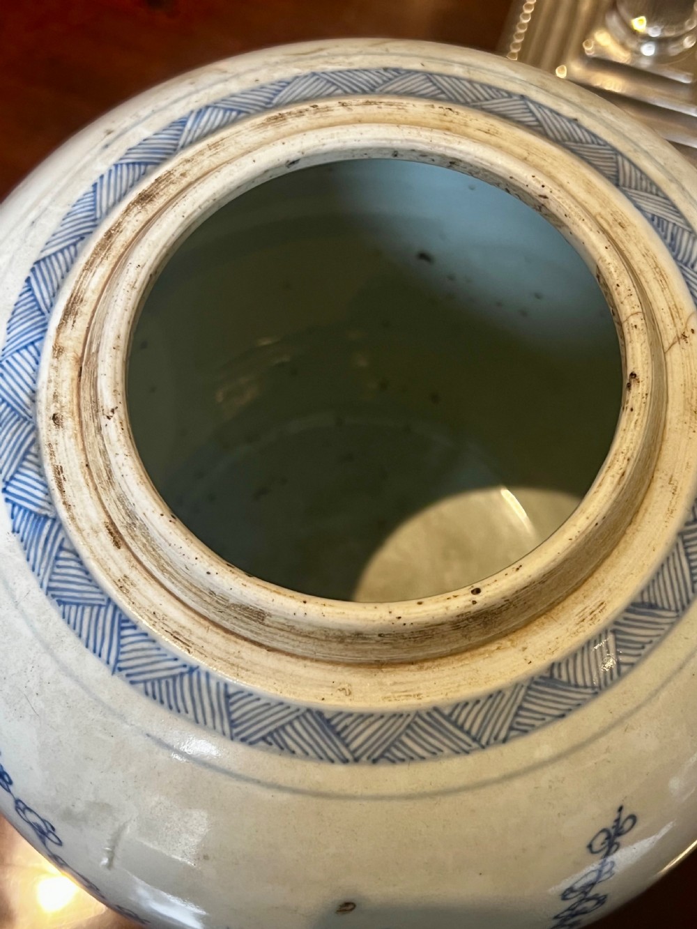 A blue and white porcelain ginger jar featuring hand-painted botanical motifs, complete with a wooden cover and resting on an intricately carved wooden stand. View VIII