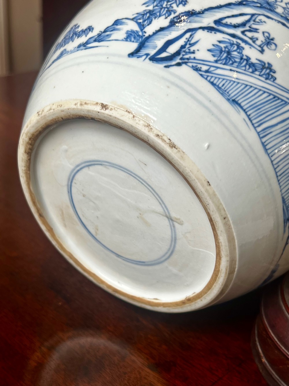 A blue and white porcelain ginger jar featuring hand-painted botanical motifs, complete with a wooden cover and resting on an intricately carved wooden stand. View IX