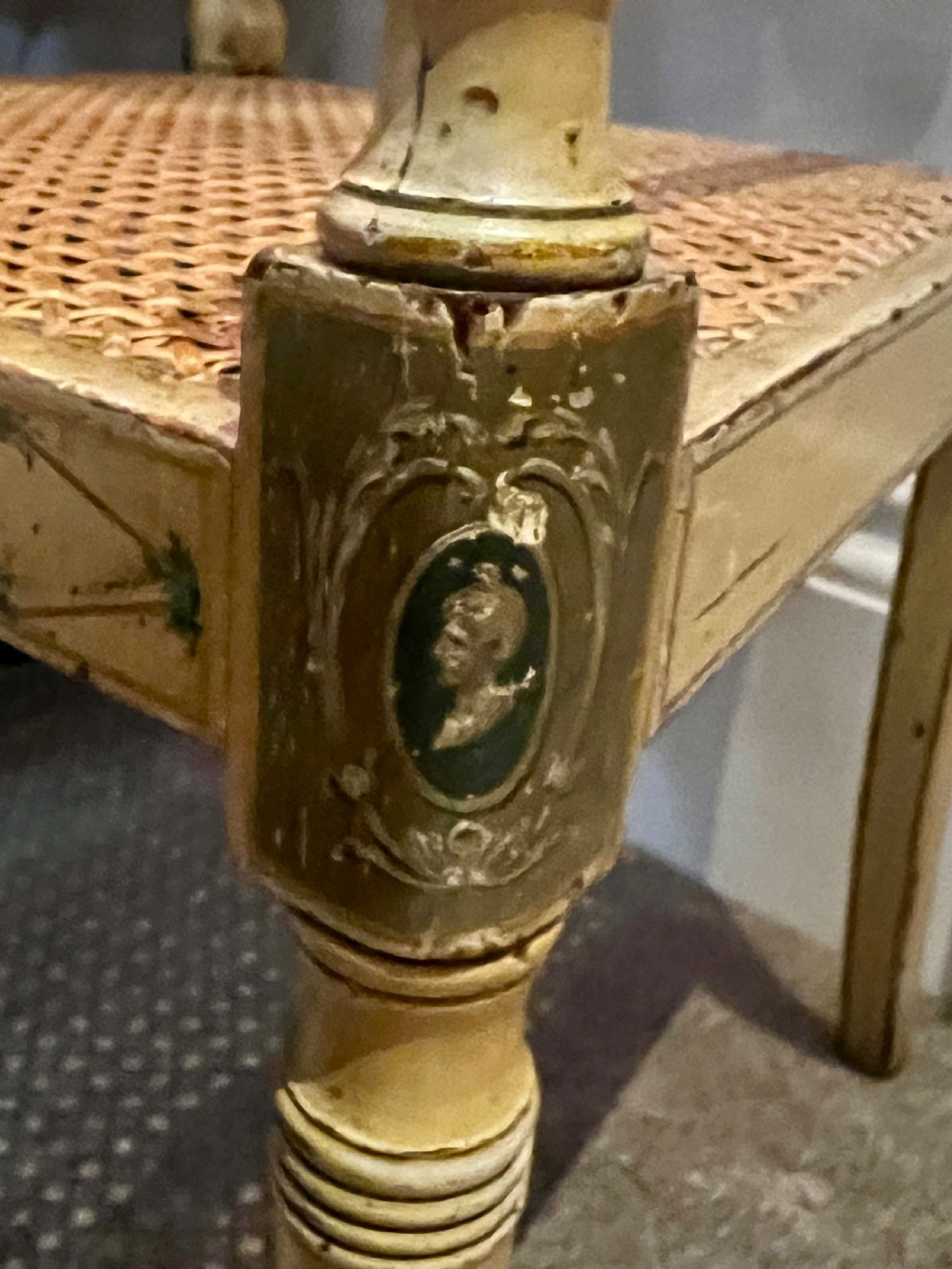 A Regency period cream painted elbow chair featuring hand-painted crest rail decoration, a geometric lattice back, sweeping arms, turned front legs, and a woven cane seat. View II