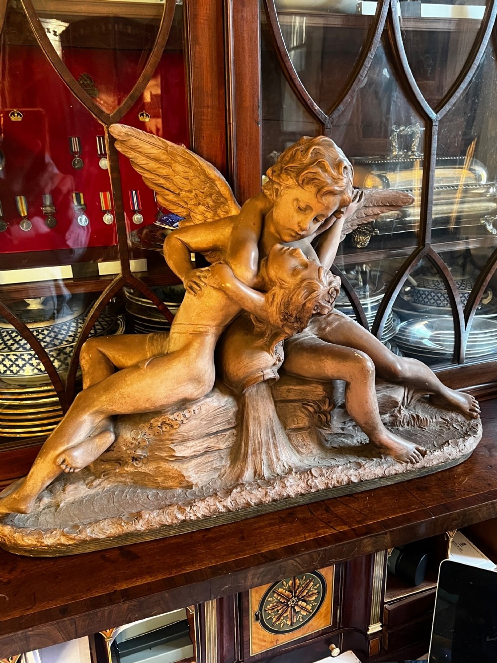 A late nineteenth-century terracotta sculpture depicting two winged mythological figures embracing beside an overturned urn on a textured base.