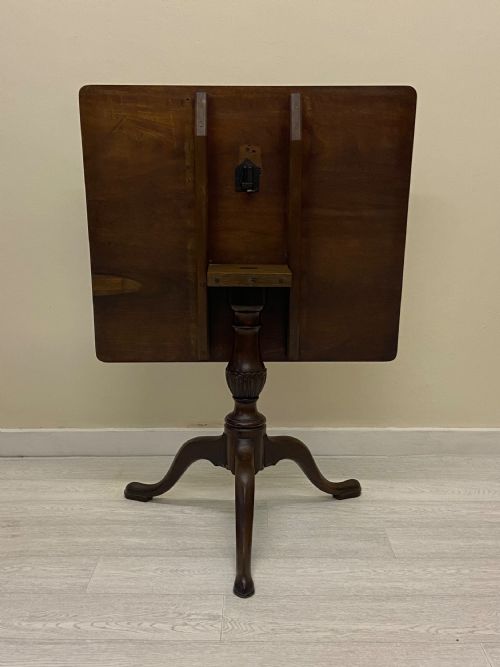 fig 5. A square dark mahogany tilt-top table featuring a central turned stem supported by three cabriole legs with pad feet.