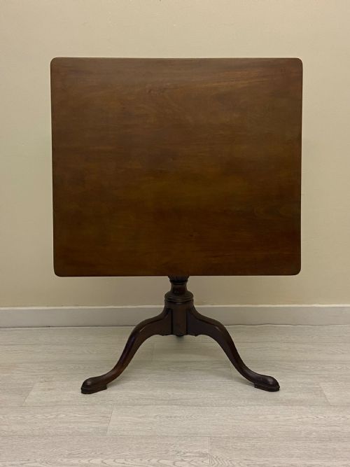 fig 4. A square dark mahogany tilt-top table featuring a central turned stem supported by three cabriole legs with pad feet.
