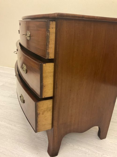 fig 5. A Victorian mahogany chest of drawers featuring three curved bow-front drawers, brass hardware, and shaped feet.