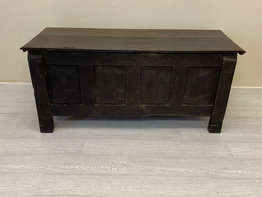 An 18th-century dark oak coffer with a flat rectangular top and four recessed front panels resting on extended stile feet.