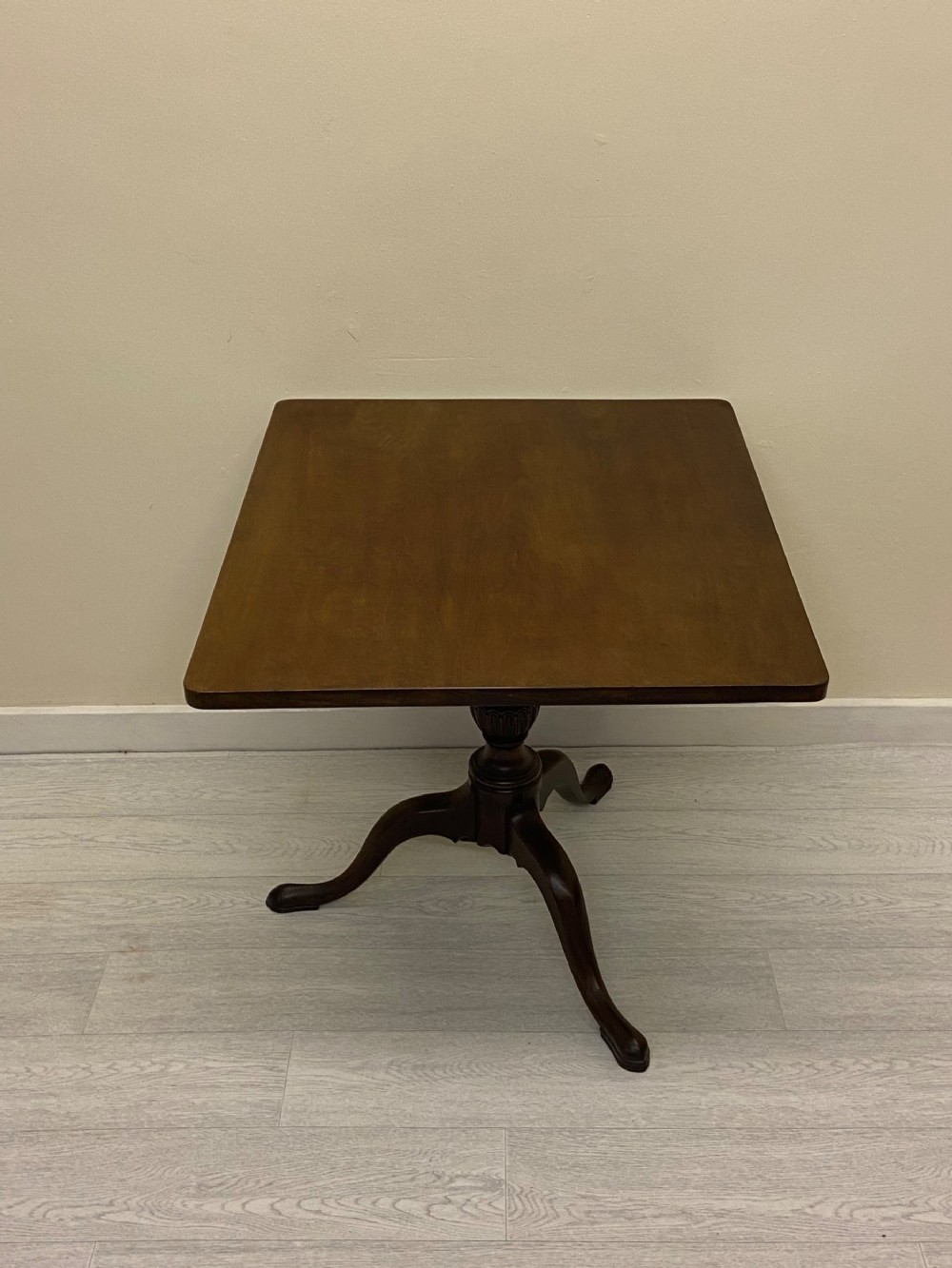 A square dark mahogany tilt-top table featuring a central turned stem supported by three cabriole legs with pad feet.