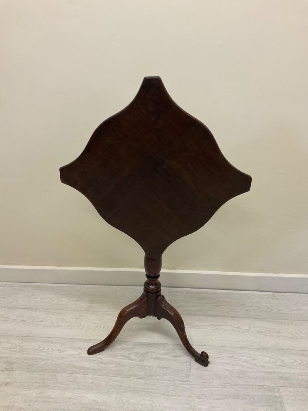 A dark mahogany Victorian tilt-top side table resting on a turned central pedestal with three cabriole legs, shown with the top secured in the vertical position.