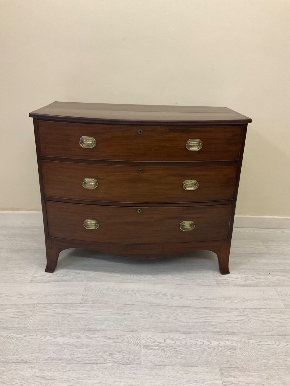 A Victorian mahogany chest of drawers featuring three curved bow-front drawers, brass hardware, and shaped feet.